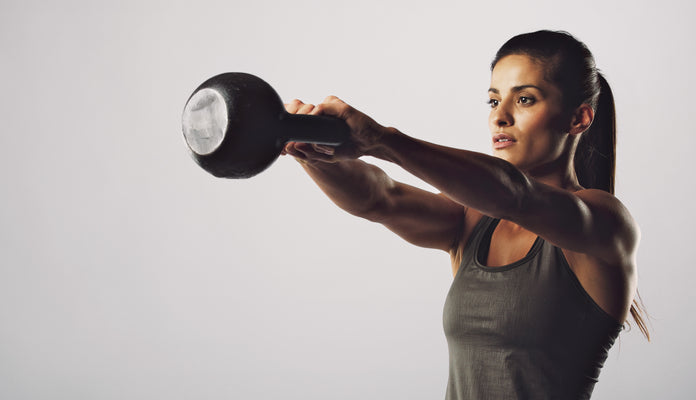 woman swinging kettlebell on a plain white background